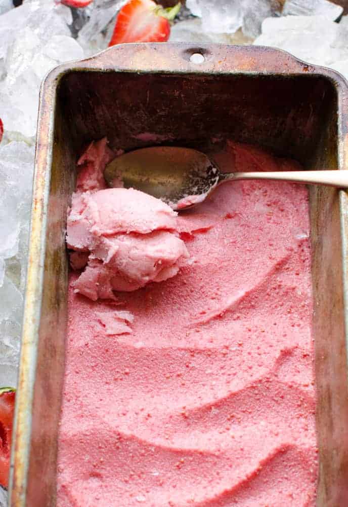 4 Ingredient Strawberry Frozen Yogurt in a loaf pan with a spoon scooping some out.