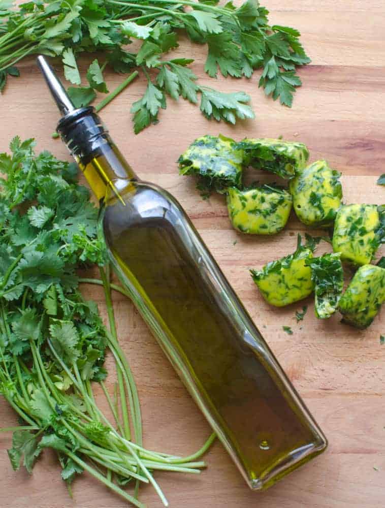 Fresh herbs, olive oil and some frozen herb bombs on a wooden cutting board.