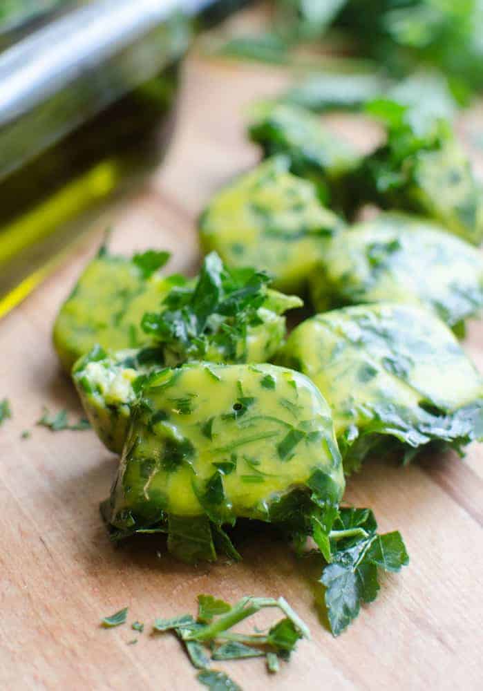 Close up of some herb bombs on a wooden cutting board with a bottle of olive oil in the background.
