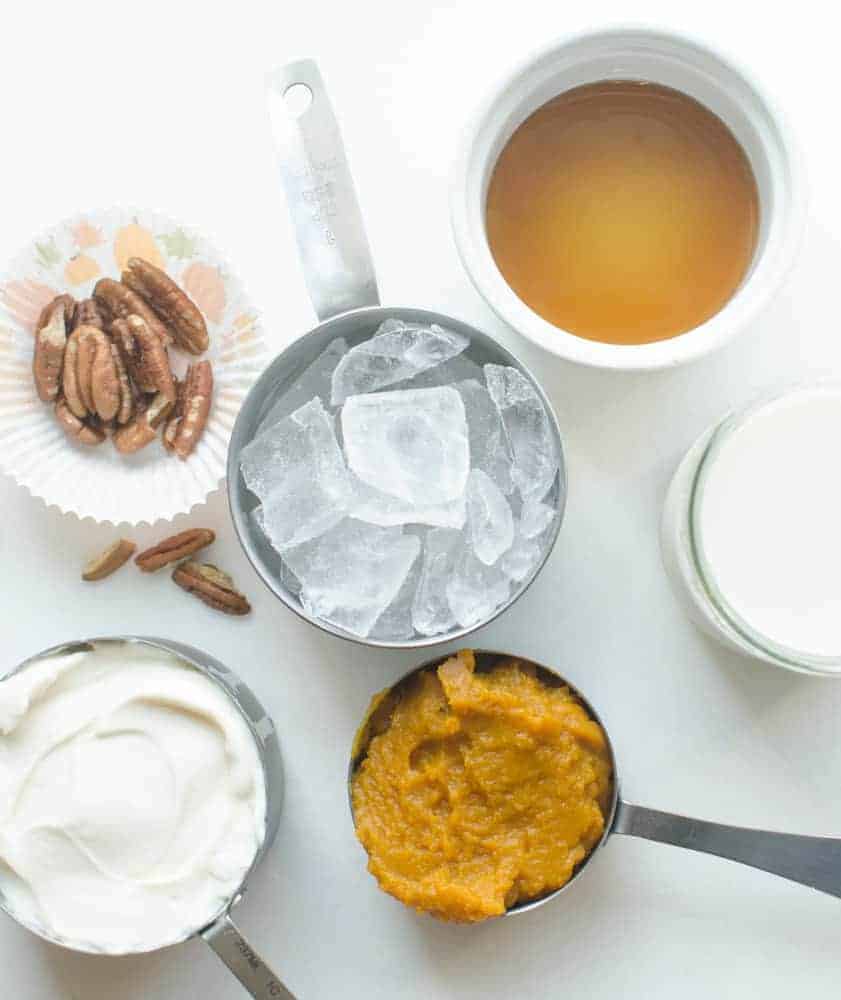 Ingredients for a Healthy Pumpkin Protein Smoothie including ice, pecan halves, plain vanilla yogurt, vanilla almond milk, maple syrup, and pumpkin purée.