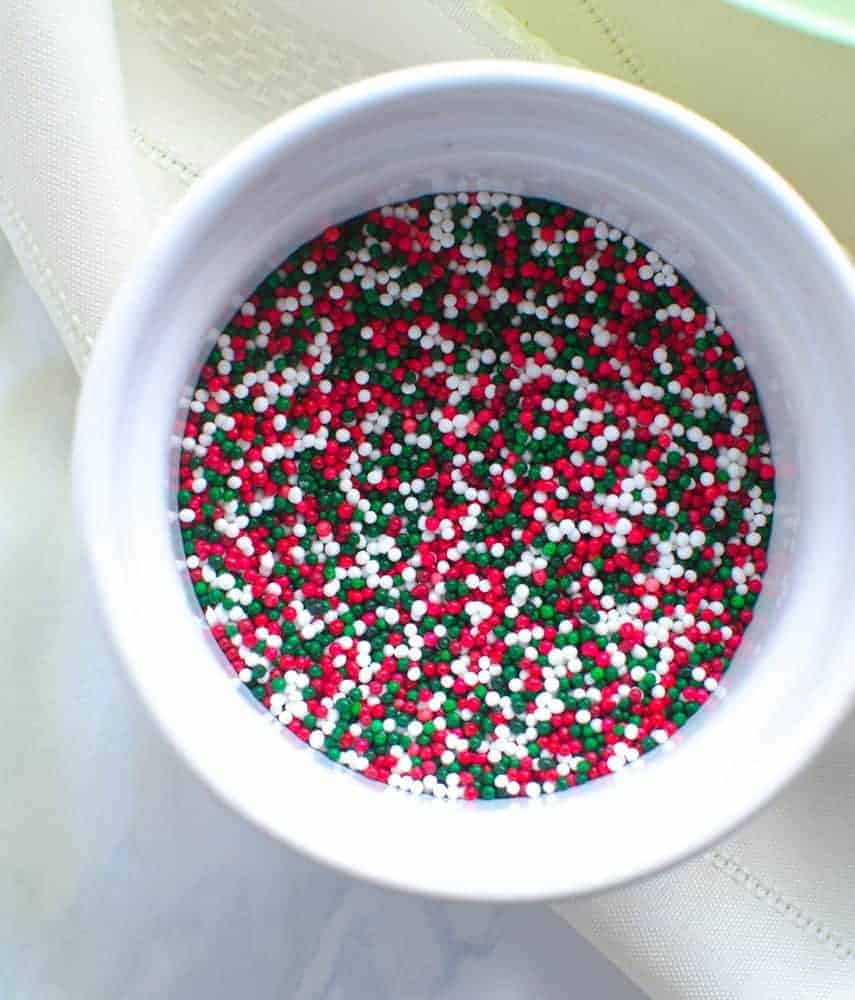 Red, green, and white small sphere-shaped sprinkles in a white bowl.