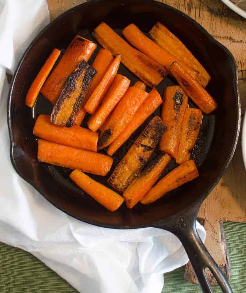 Pan-seared carrots in a cast iron pan on a wooden table.