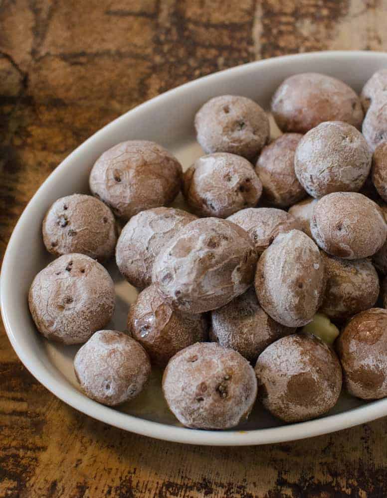A white oval plate filled with small, round, salt-crusted potatoes on a wooden surface—perfect as one of your Thanksgiving dinner side dishes.