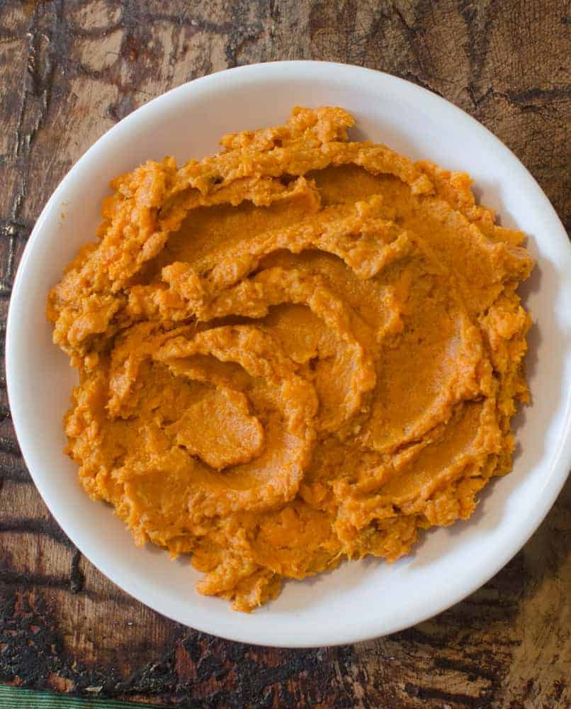 Mashed roasted sweet potatoes in a white bowl on a wooden table.