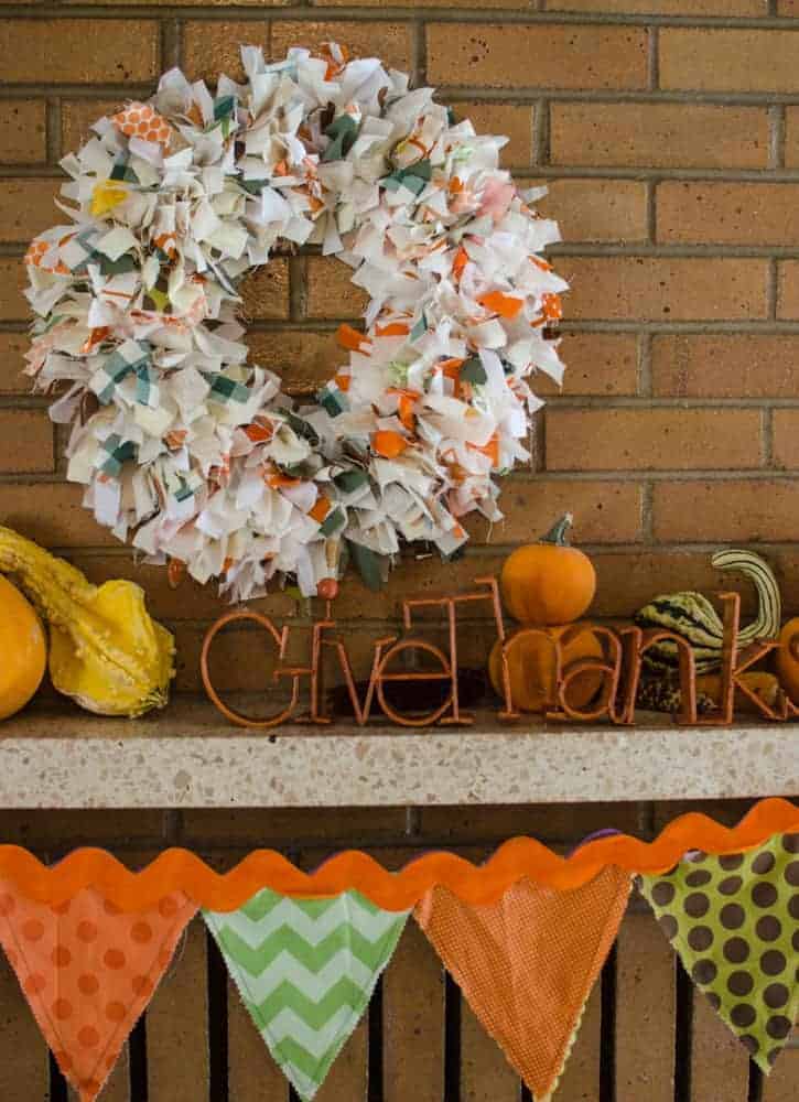 DIY Fall Rag Wreath hanging on a brick fireplace with gourds and a Give Thanks sign on the mantel.