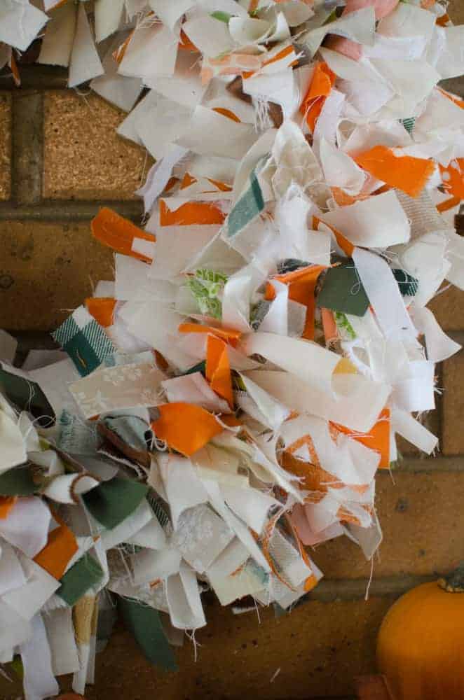 A DIY Fall Rag Wreath hanging on a brick fireplace.