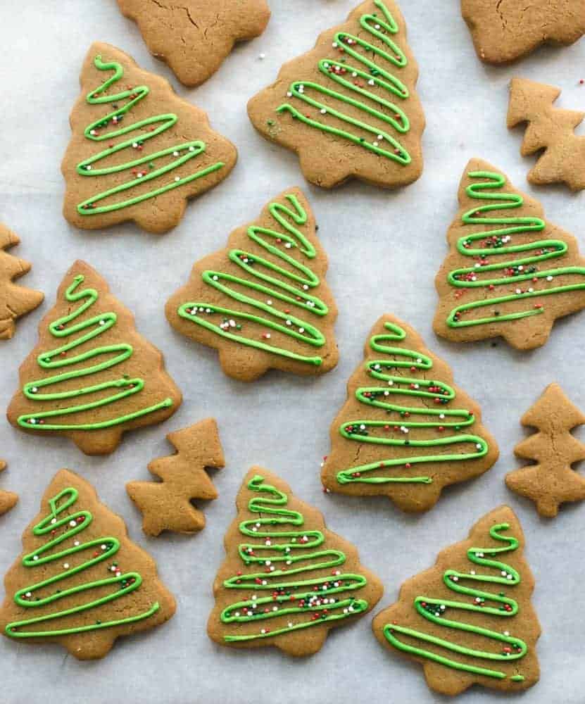 Gingerbread cookies cut out like trees and decorated with green icing and sprinkles on white paper.