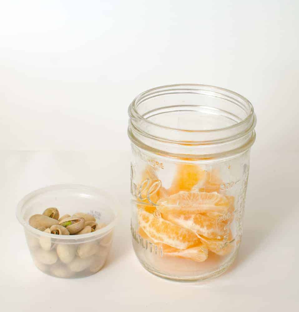 A peeled mandarin orange and some pistachios in a Mason jar.