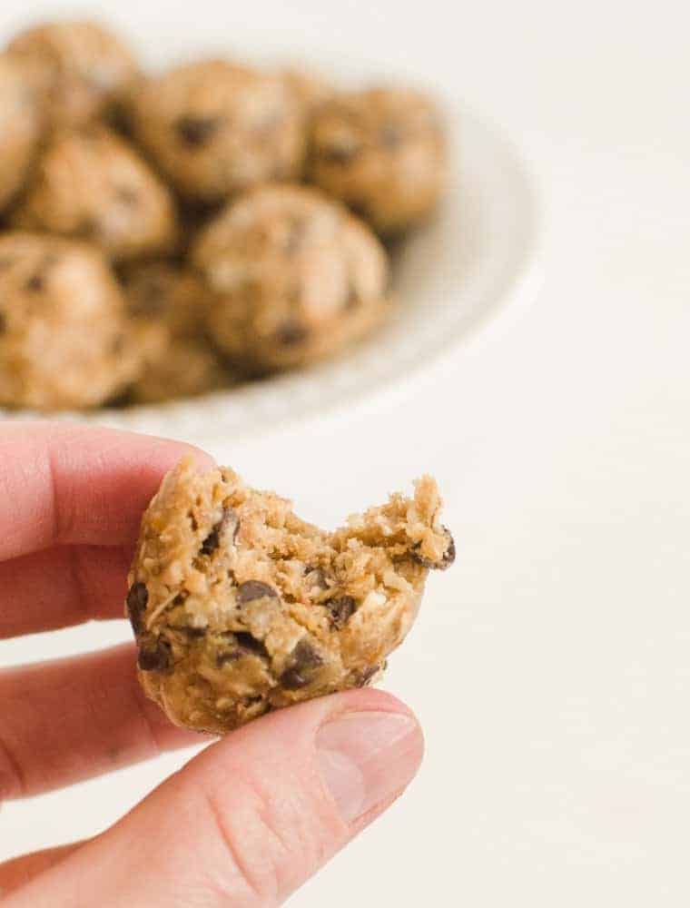 A hand holding a Peanut Butter Chocolate Chip Oatmeal Energy Ball with a bite taken out of it.