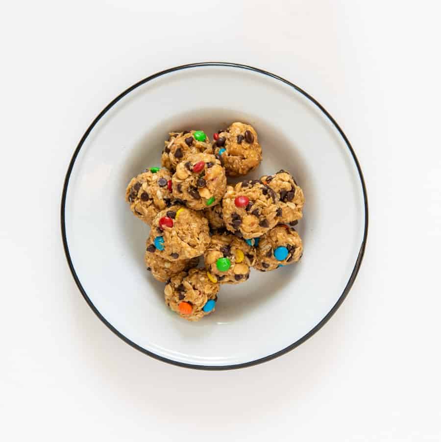 A dozen monster cookie no-bake oatmeal energy balls in a white enamel bowl with a black rim.