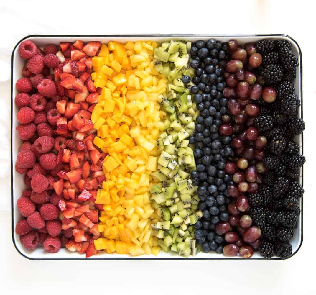 Fruit to make healthy rainbow popsicles including raspberries, strawberries, mango, pineapple, kiwi, blueberries, purple grapes, and blackberries.