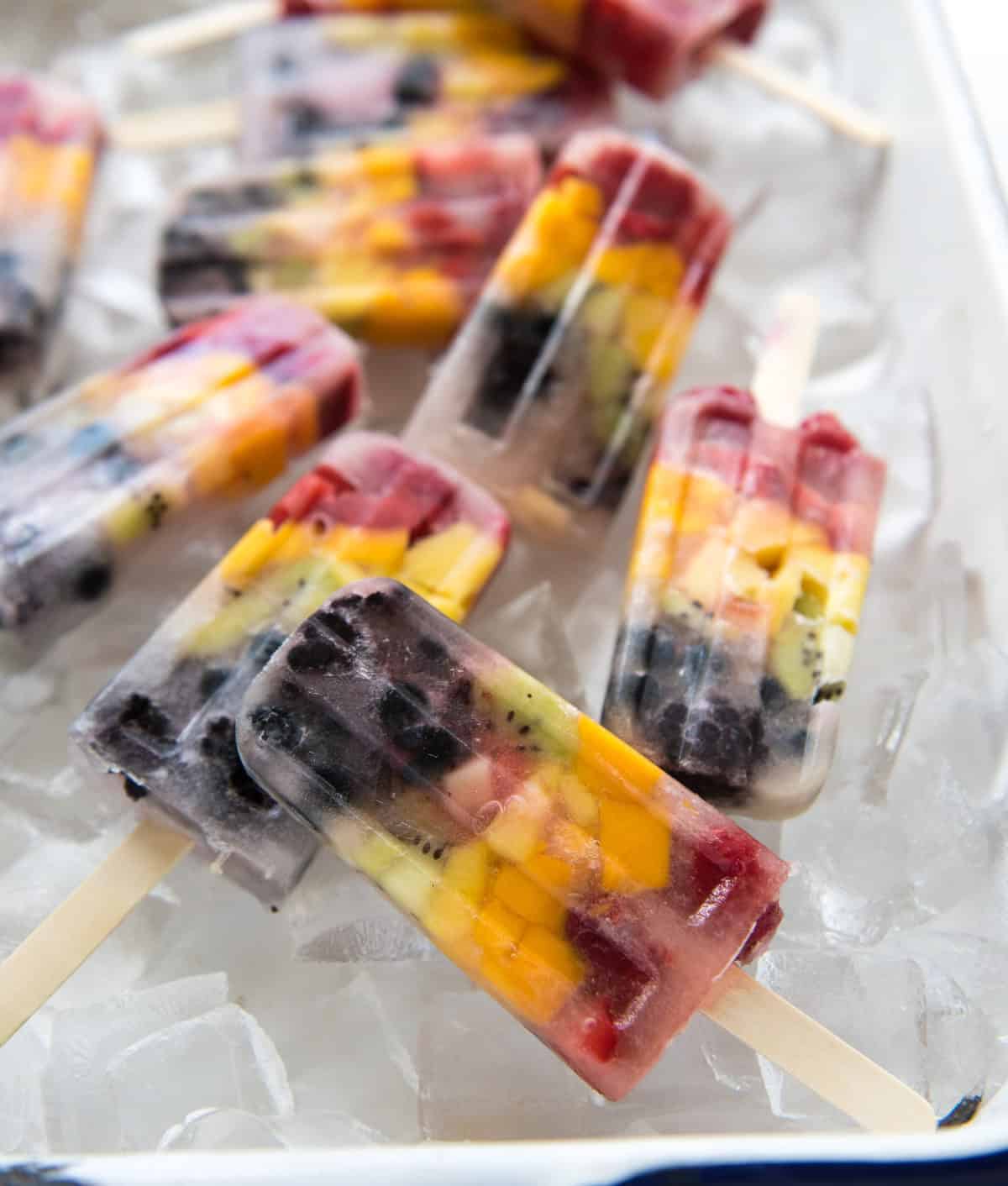 A close-up of a healthy rainbow popsicle on a bed of ice in a white enamelware pan.
