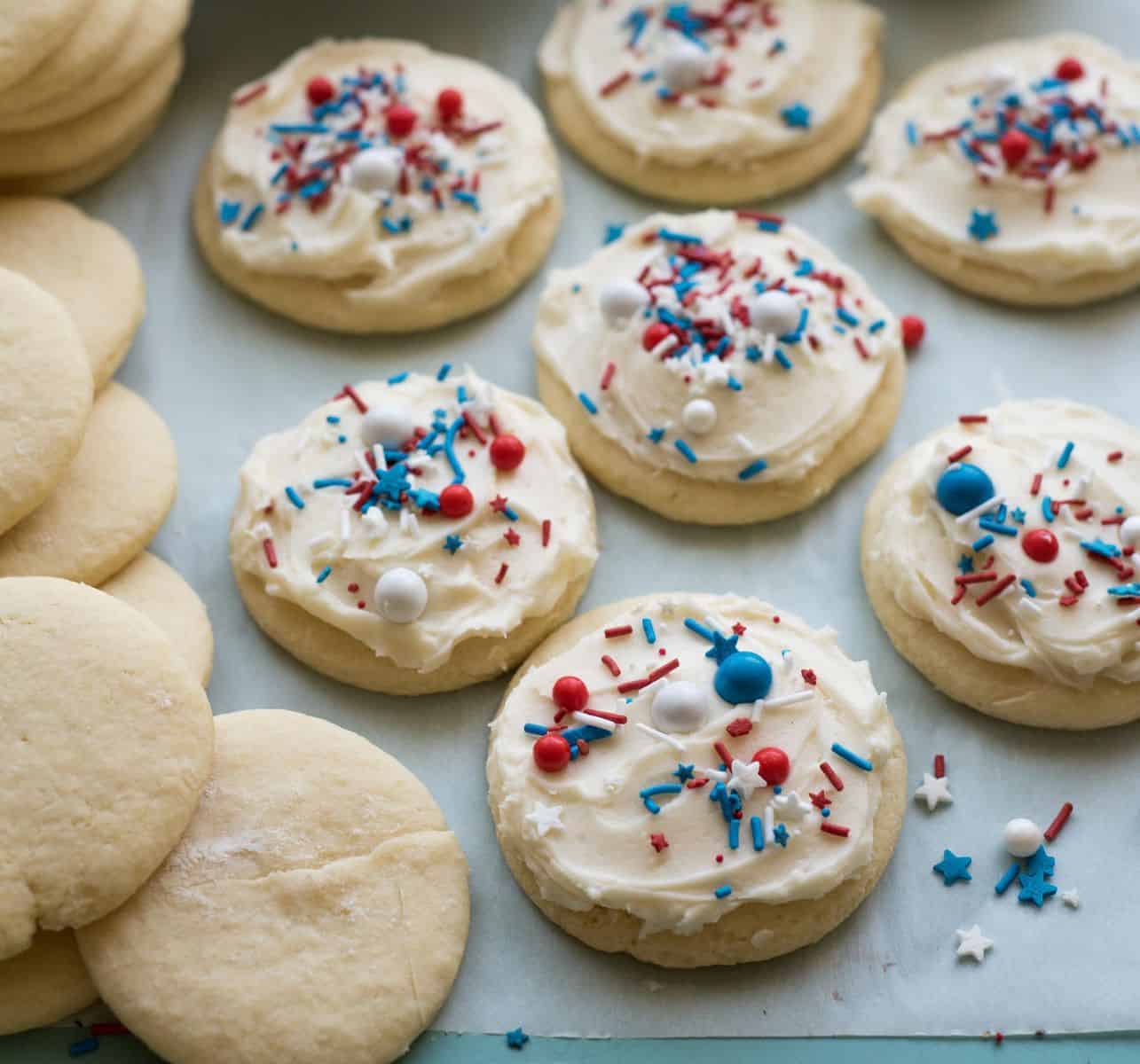 A pile of unfrosted sugar cookies next to 7 of the Best 4th of July Cookies on the Block frosted.