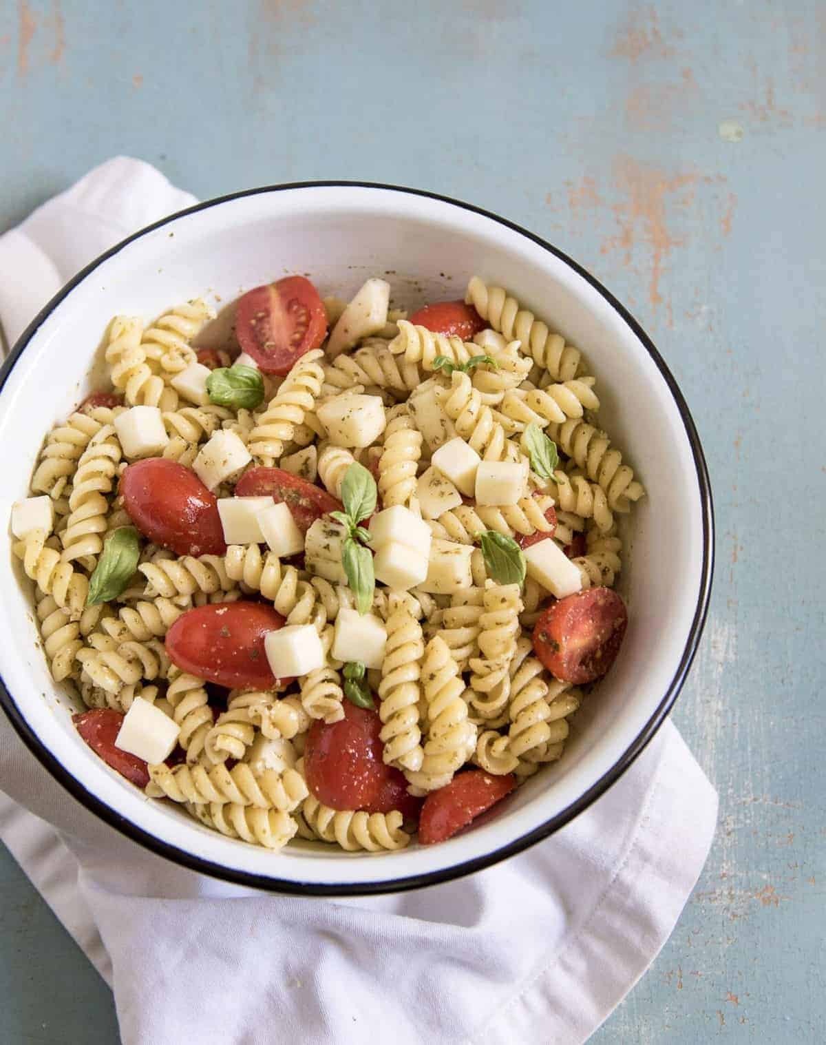 Quick & Easy Pesto Pasta Salad in a white enamelware bowl with a black rim resting on a white napkin.