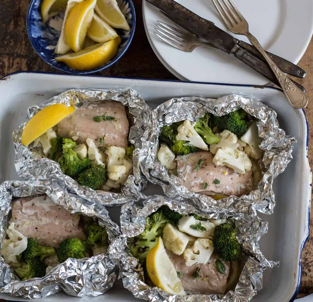 Top view of a pan with four salmon packs with lemon wedges on the side.