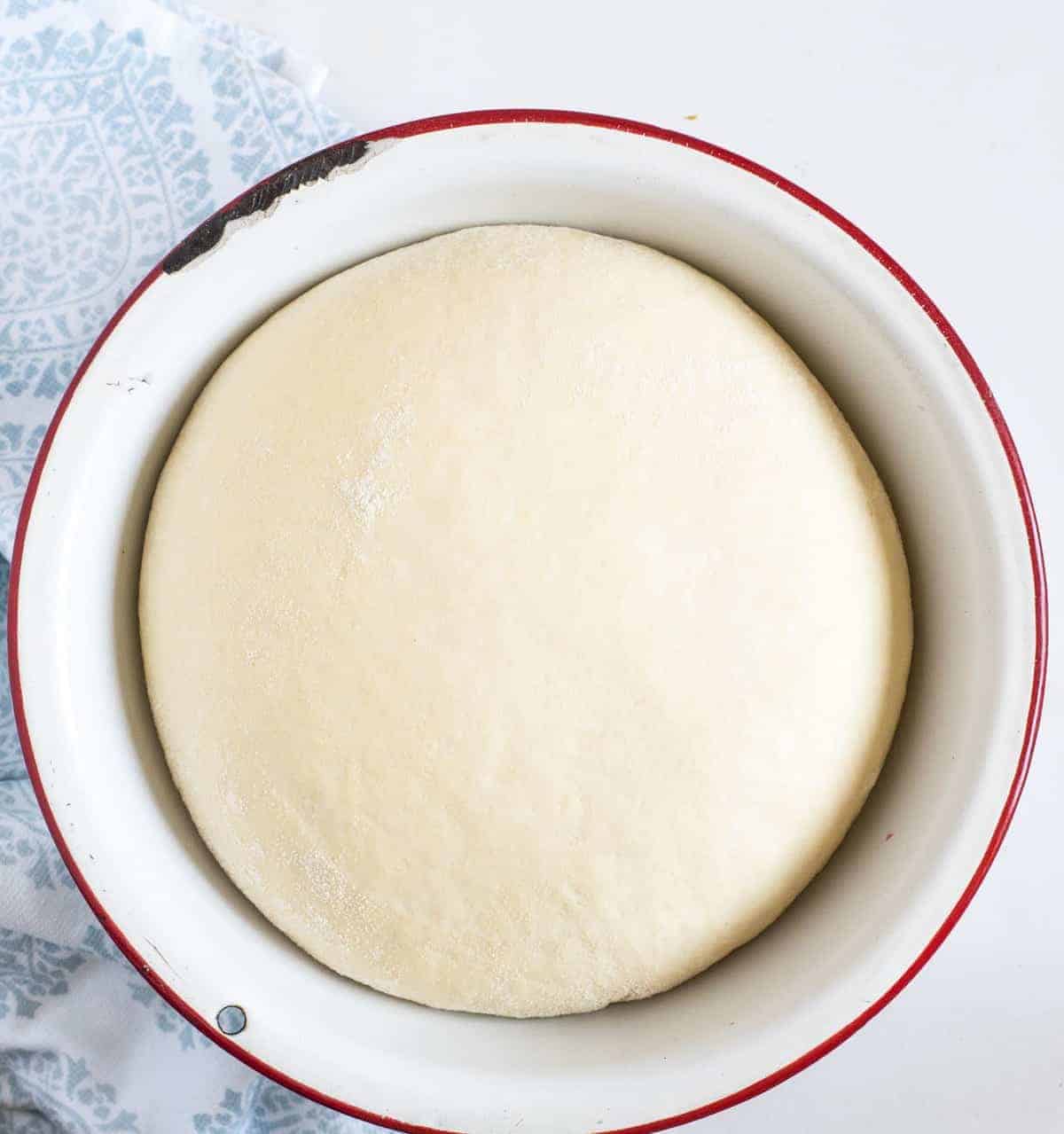 Top view of a ball of risen pizza dough in a bowl.
