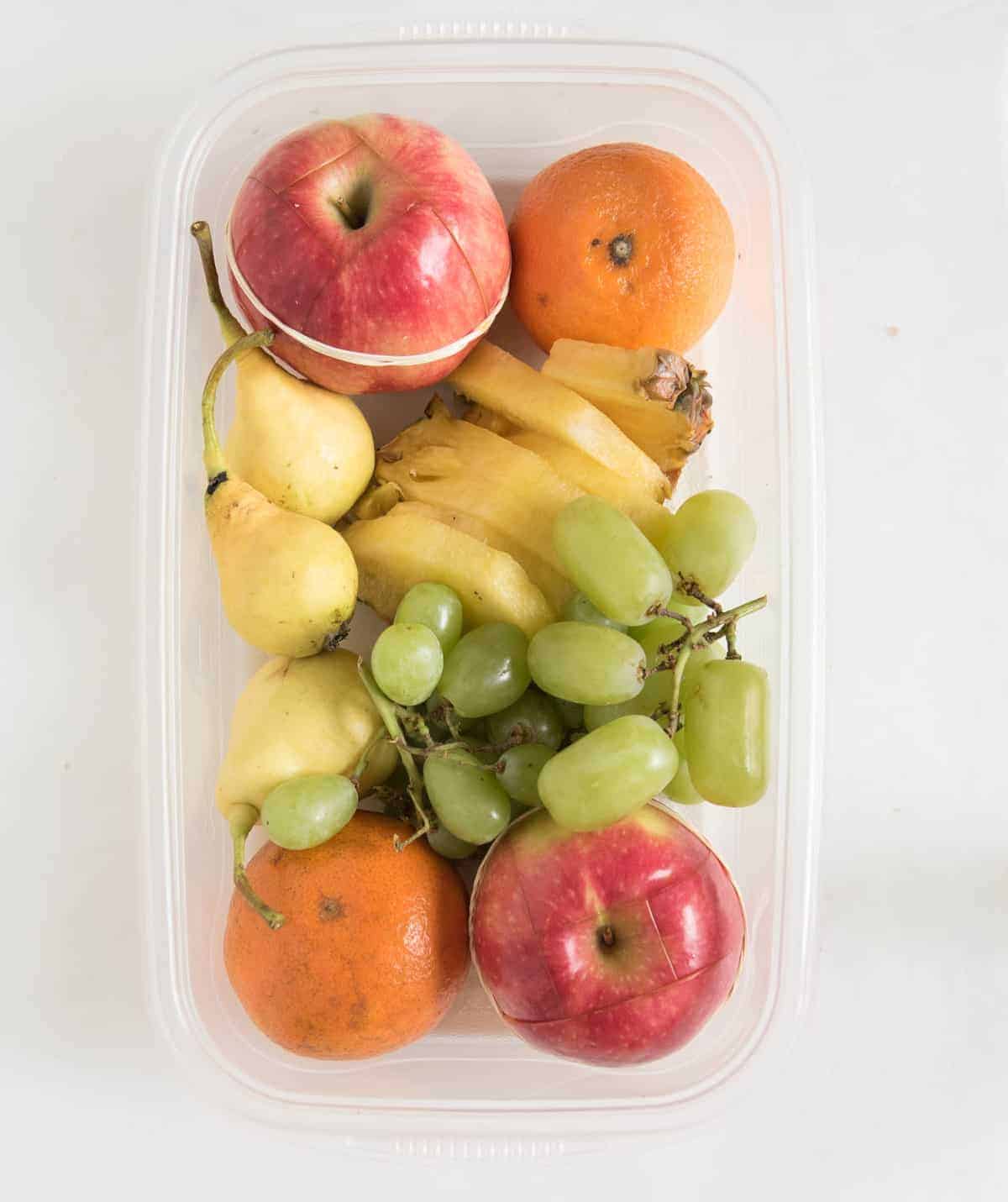 assorted fruit in a clear tupperware bowl.