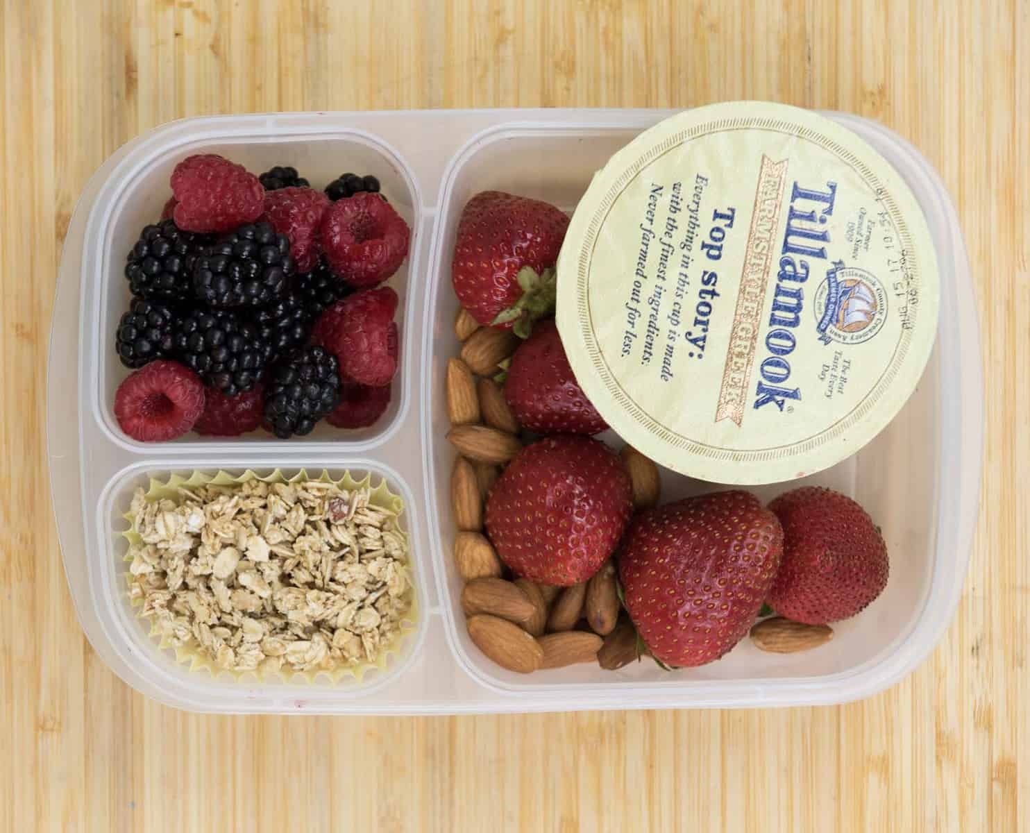 Top view of a lunch box with Yogurt, Mixed berries, Strawberries + almonds, and Granola.