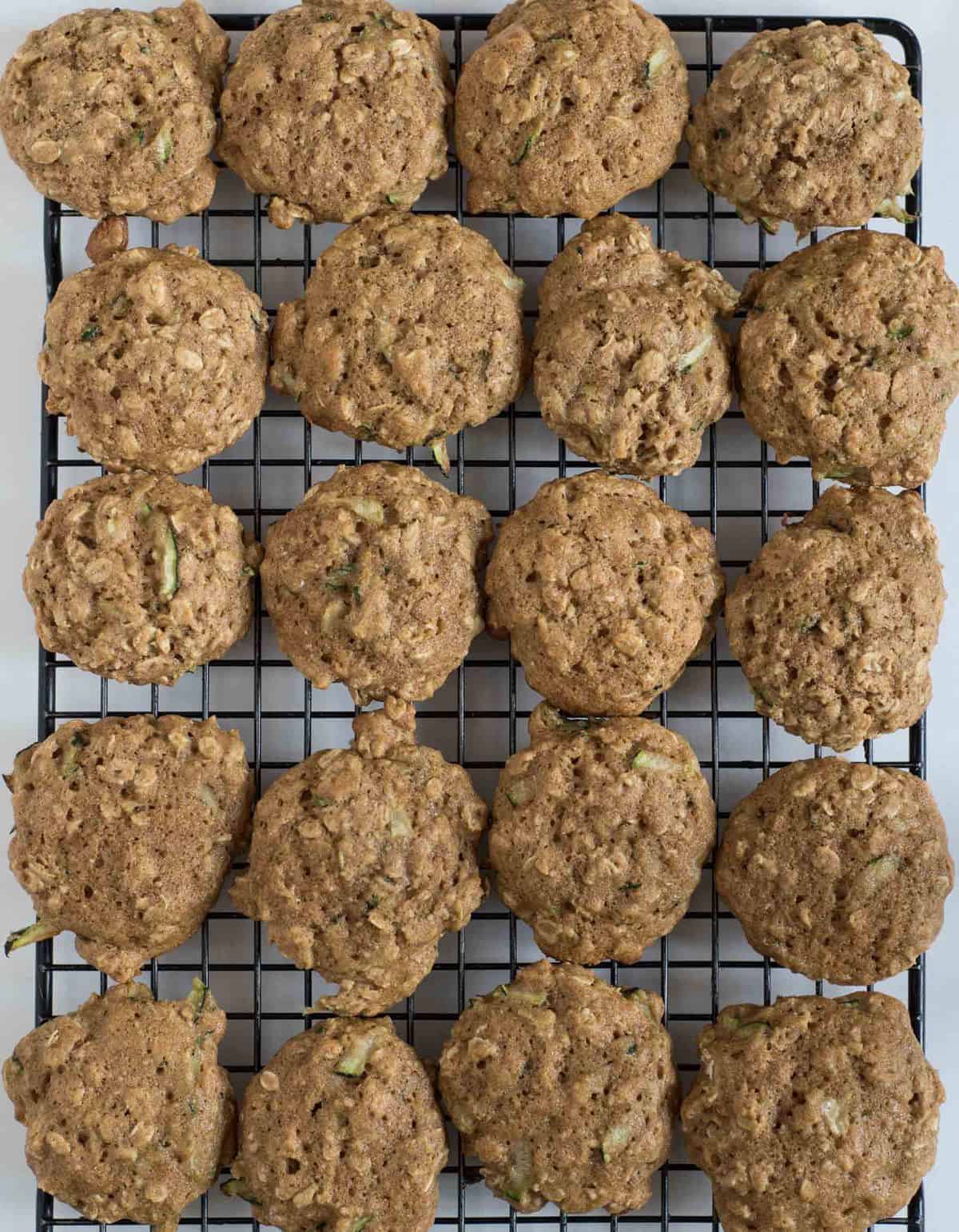 Two dozen baked zucchini oatmeal cookies on a black wire cooling rack.