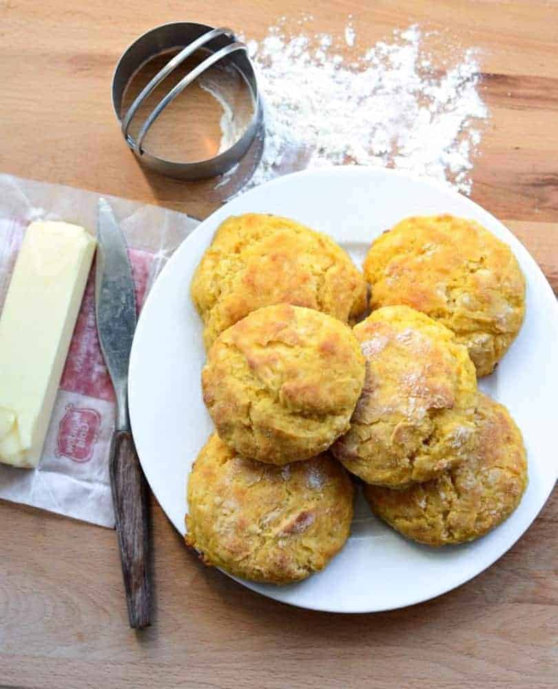 Sweet Potato Biscuits on a white plate next to butter and a biscuit cutter on a butcher block counter.
