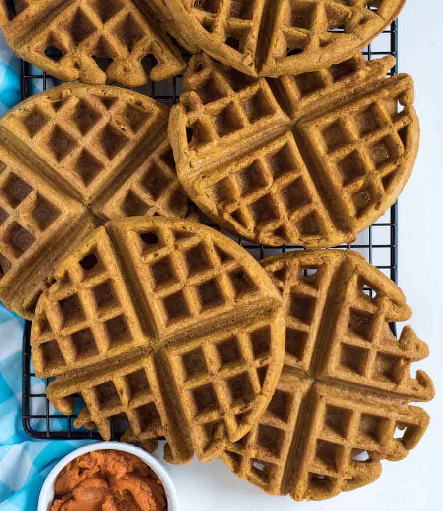 Top view of Whole Wheat Pumpkin Waffles on a cooling rack next to a bowl of pumpkin puree.