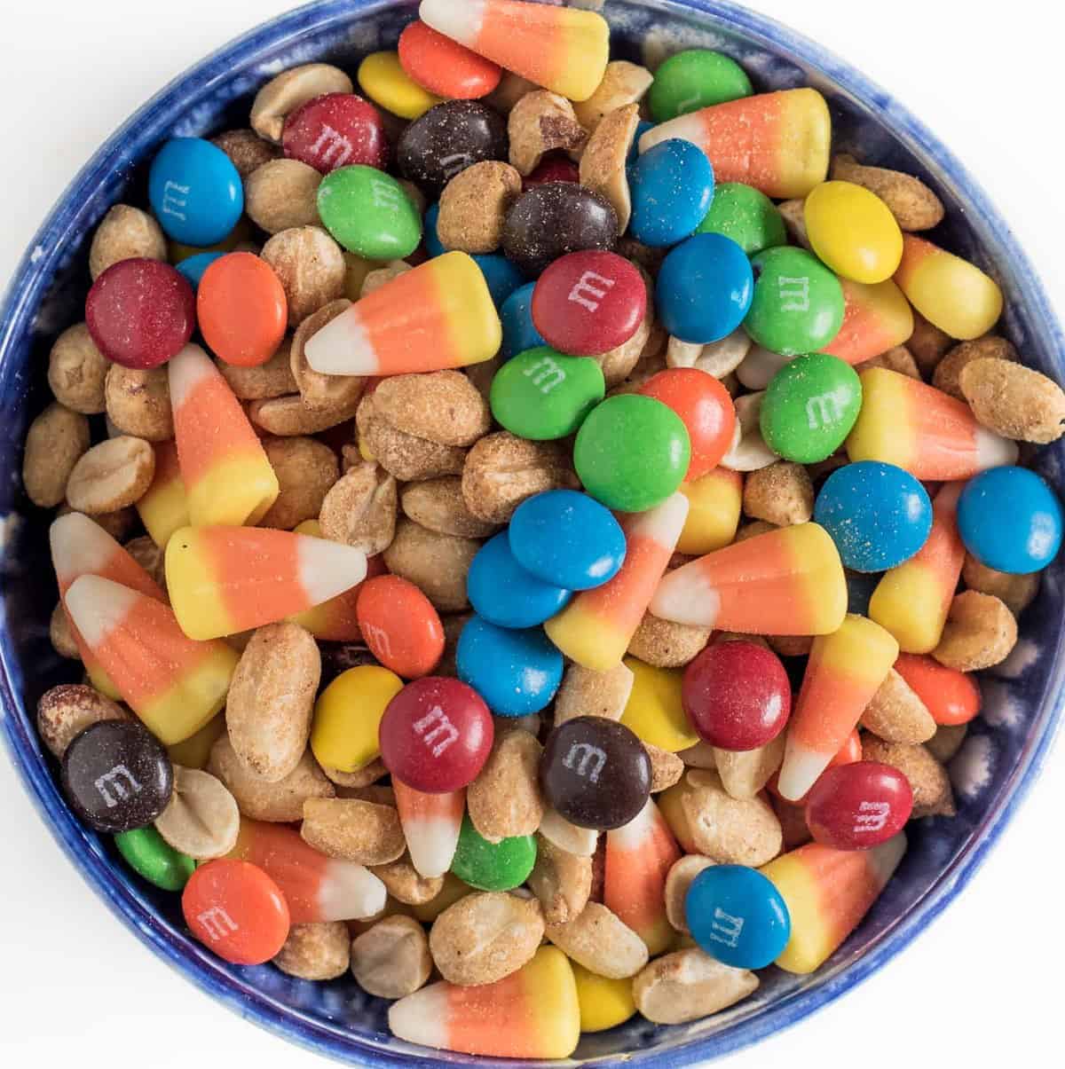 Candy corn snack mix made with M&Ms, roasted peanuts, and candy corn in a blue bowl.