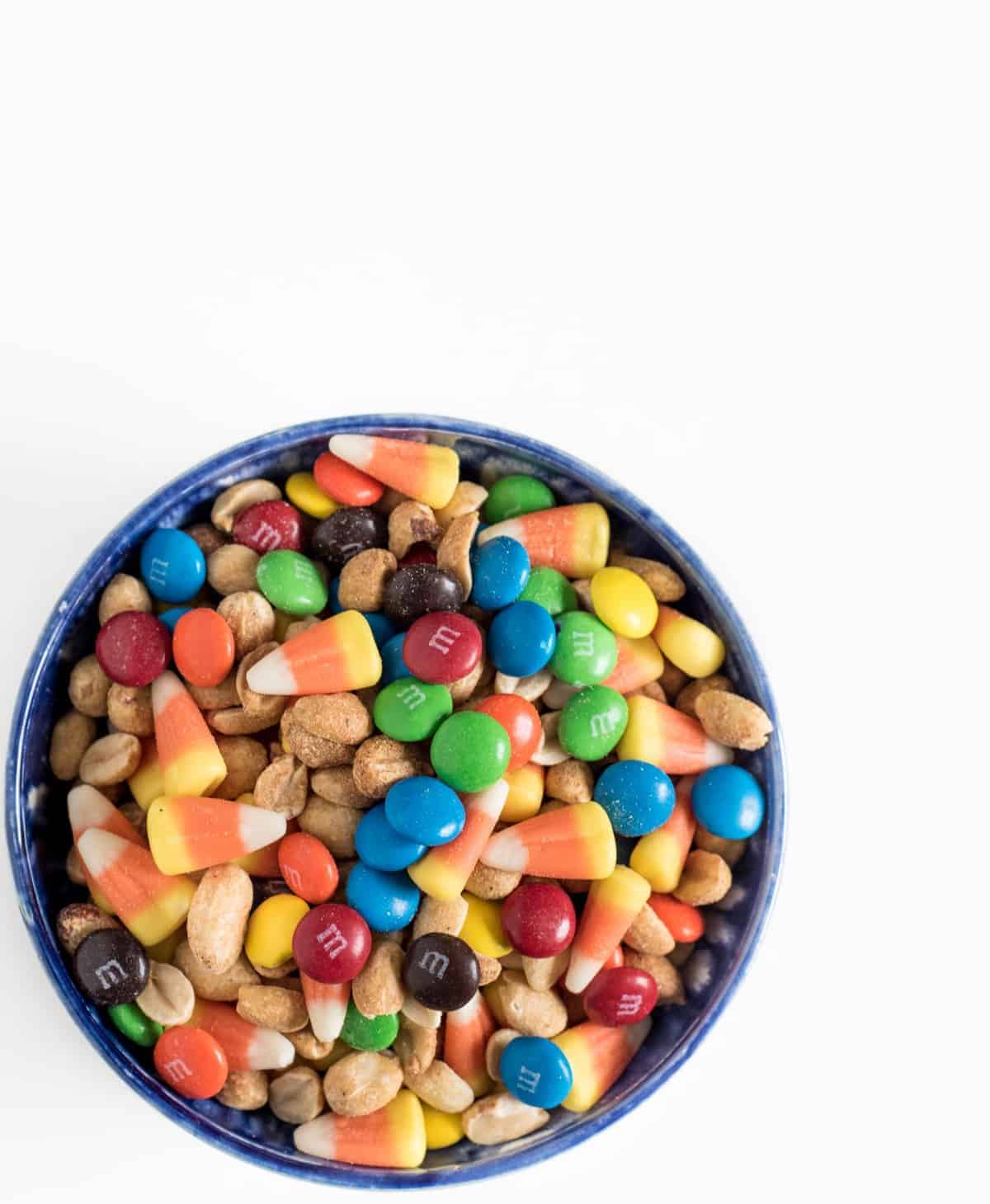 Candy corn snack mix made with M&Ms, roasted peanuts, and candy corn in a blue bowl.