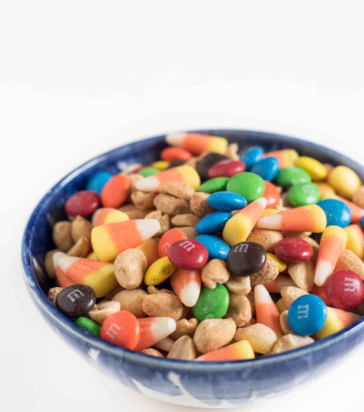 Candy corn snack mix made with M&Ms, roasted peanuts, and candy corn in a blue bowl.