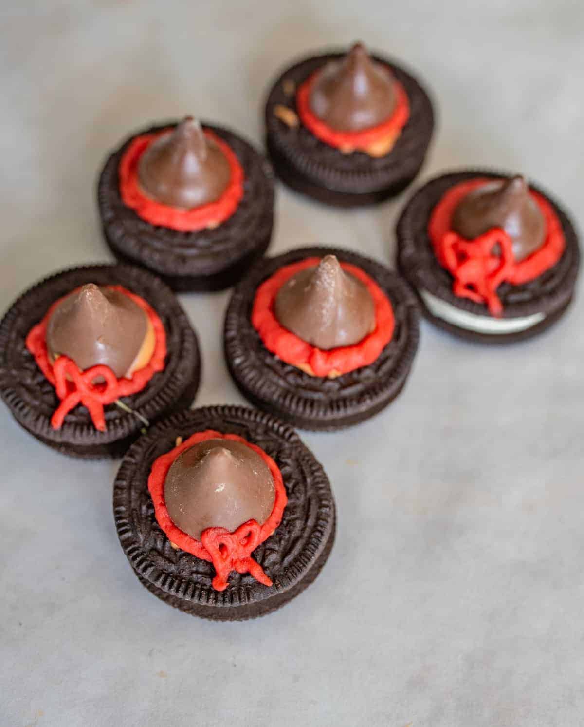 Six chocolate cookies topped with chocolate kisses and decorated with red and orange icing, arranged on a light-colored surface to resemble little hats—perfect for creative lunch box ideas.