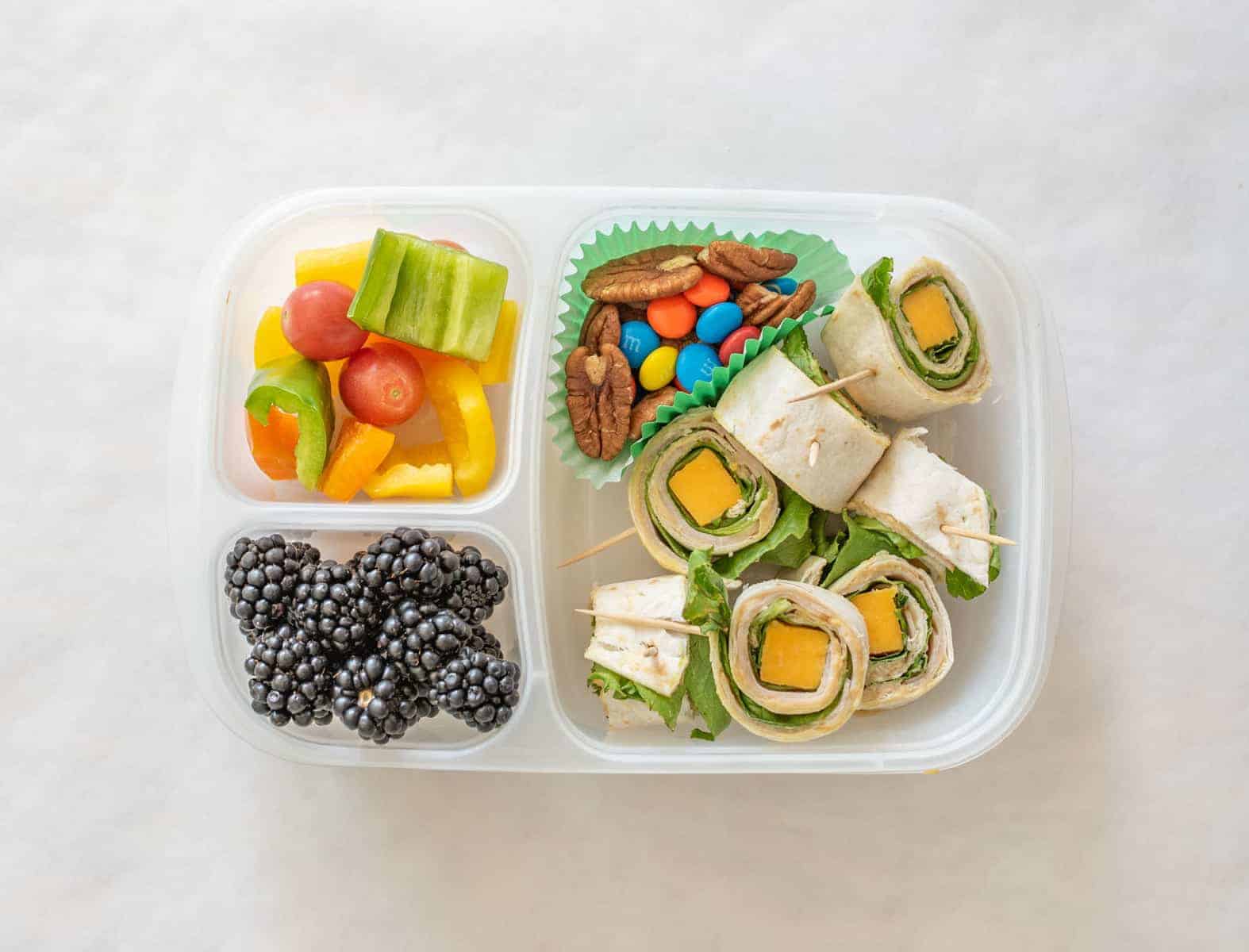 a container with berrys, pinrolls and veggies.
