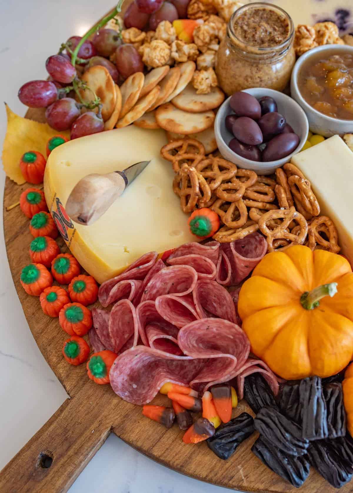 Fun and festive Halloween Cheese board made with simple cheese, crackers, pumpkins for garnish, and or coarse, lots of Halloween candy.