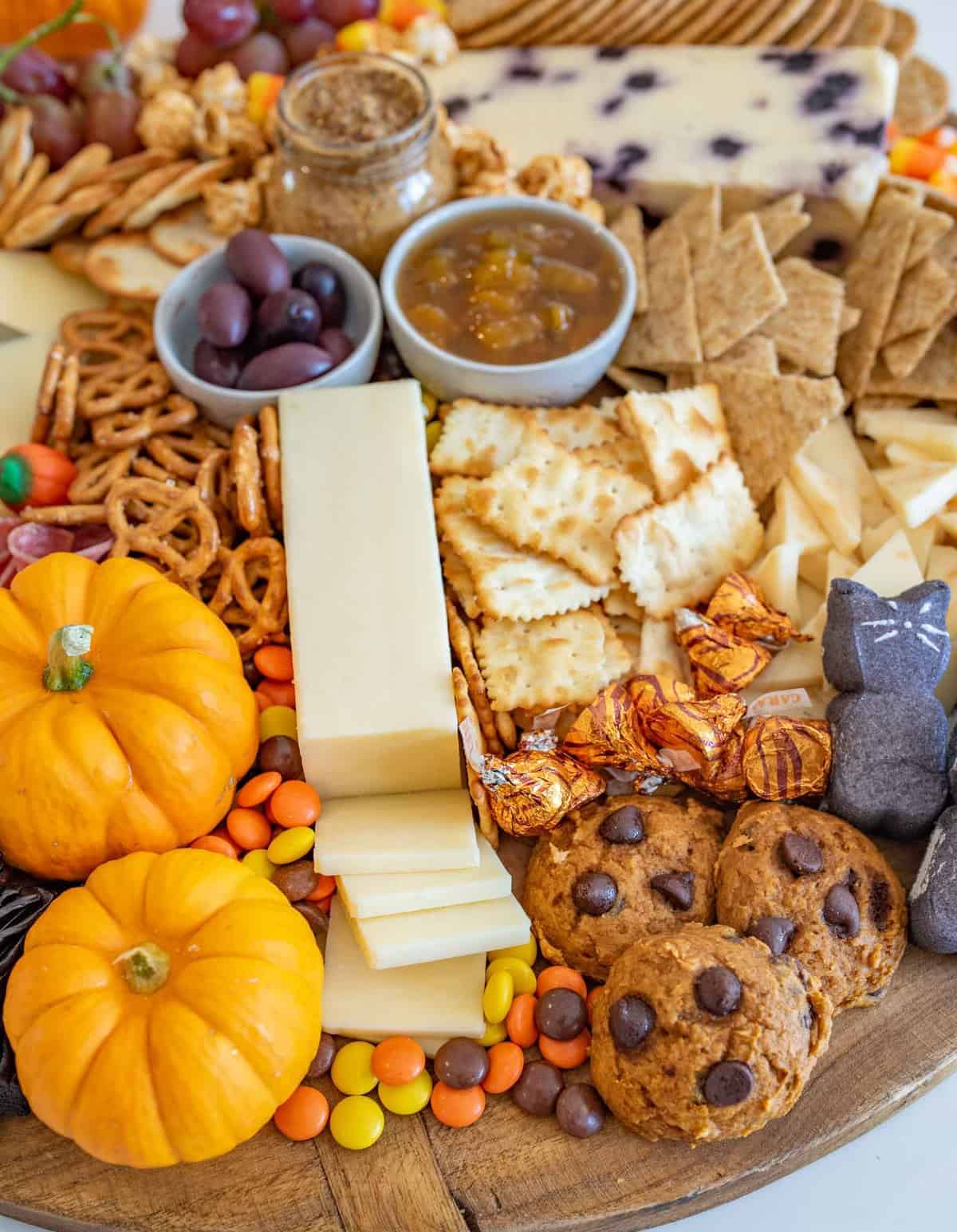 Fun and festive Halloween Cheese board made with simple cheese, crackers, pumpkins for garnish, and or coarse, lots of Halloween candy.