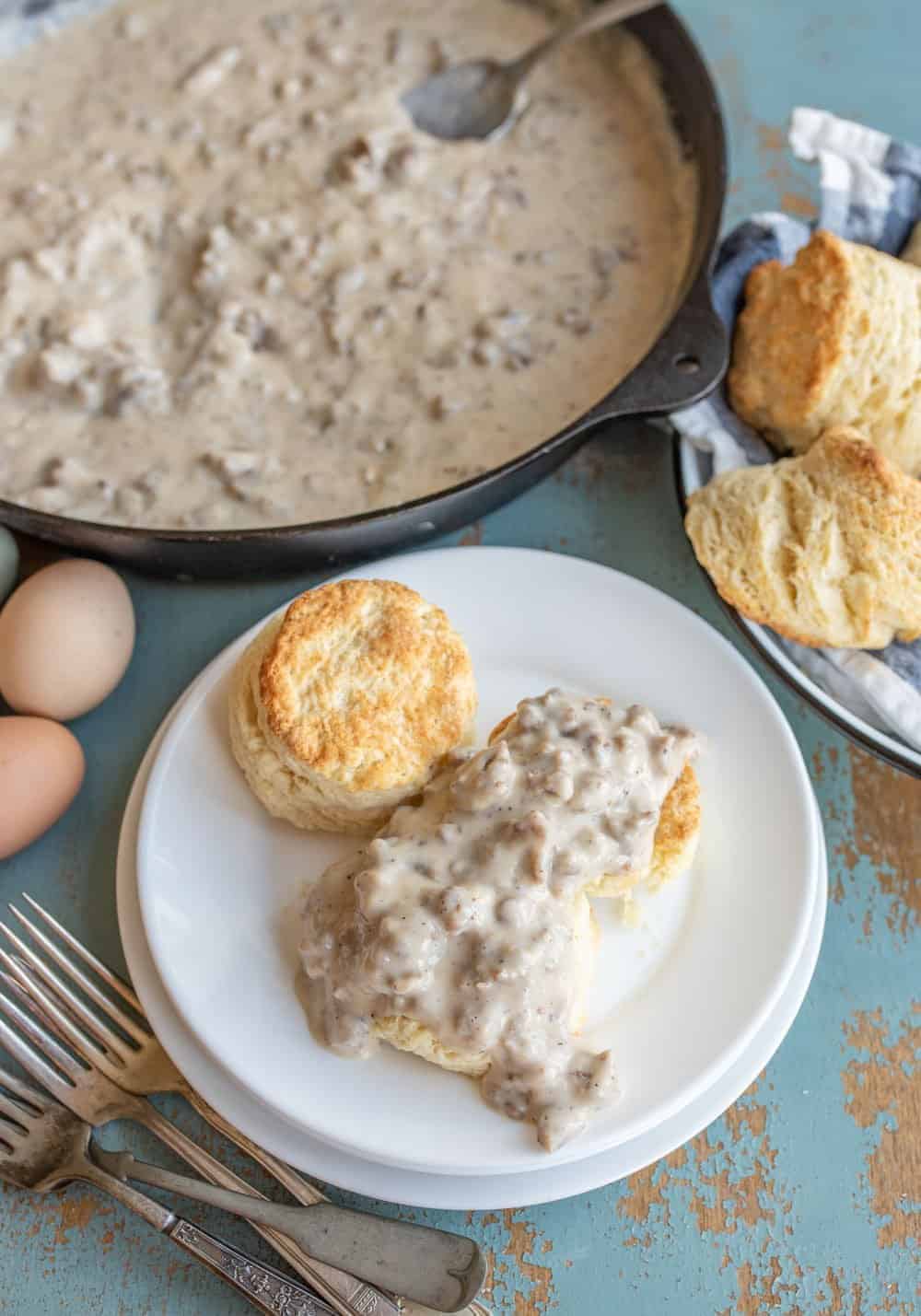 cast iron skillet with sausage gravy and a white plate with a biscuit and gravy.