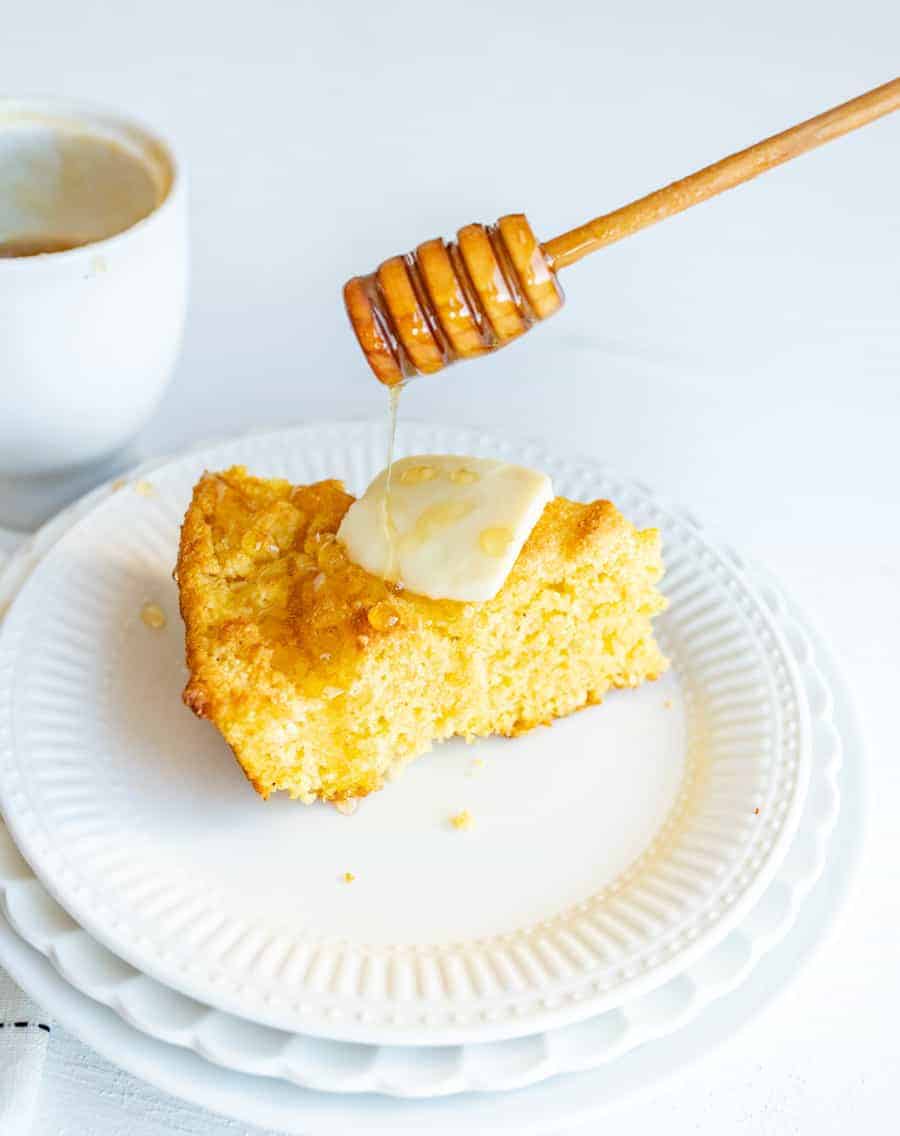 cut of cornbread on plate with butter and honey on top.