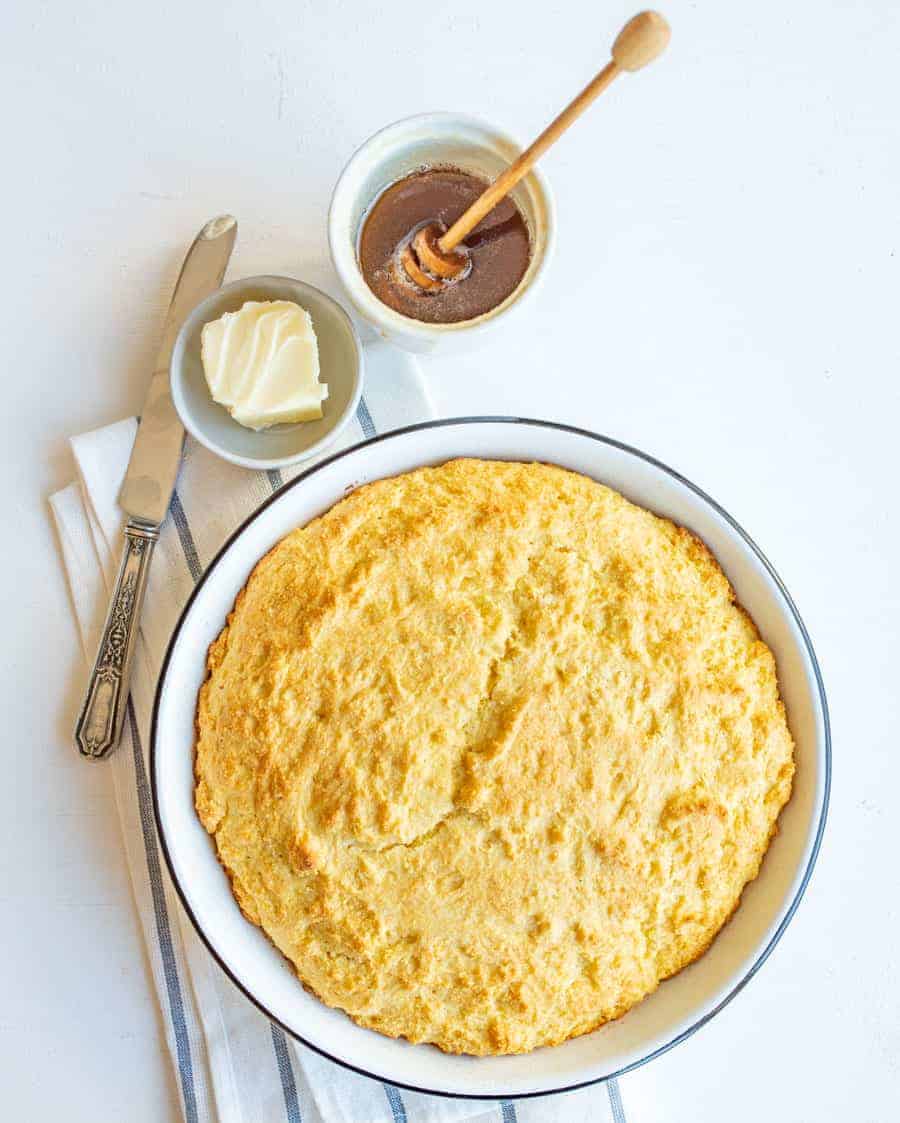 easy sour cream cornbread in round white dish with butter, honey, and butterknife.