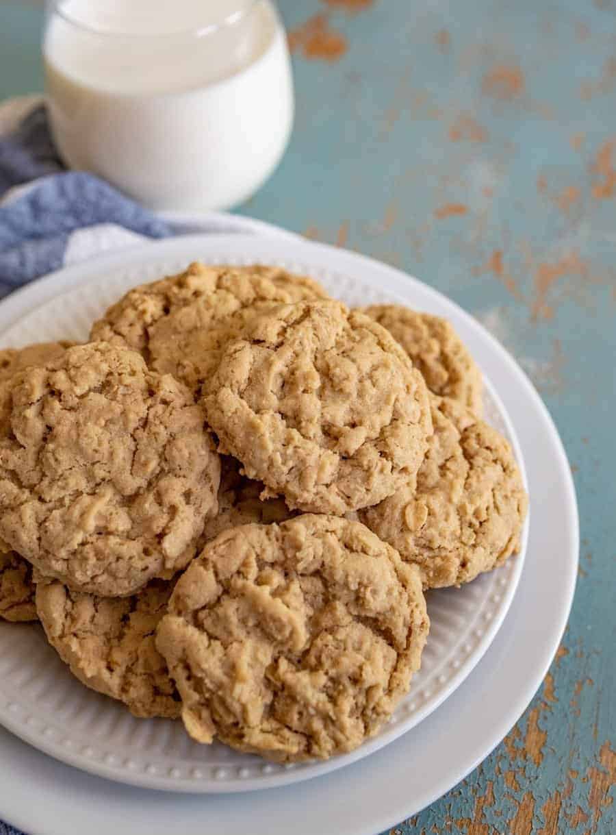 A white plate piled with several homemade treats from your favorite easy oatmeal cookies recipe sits on a rustic blue surface, with a glass of milk in the background.