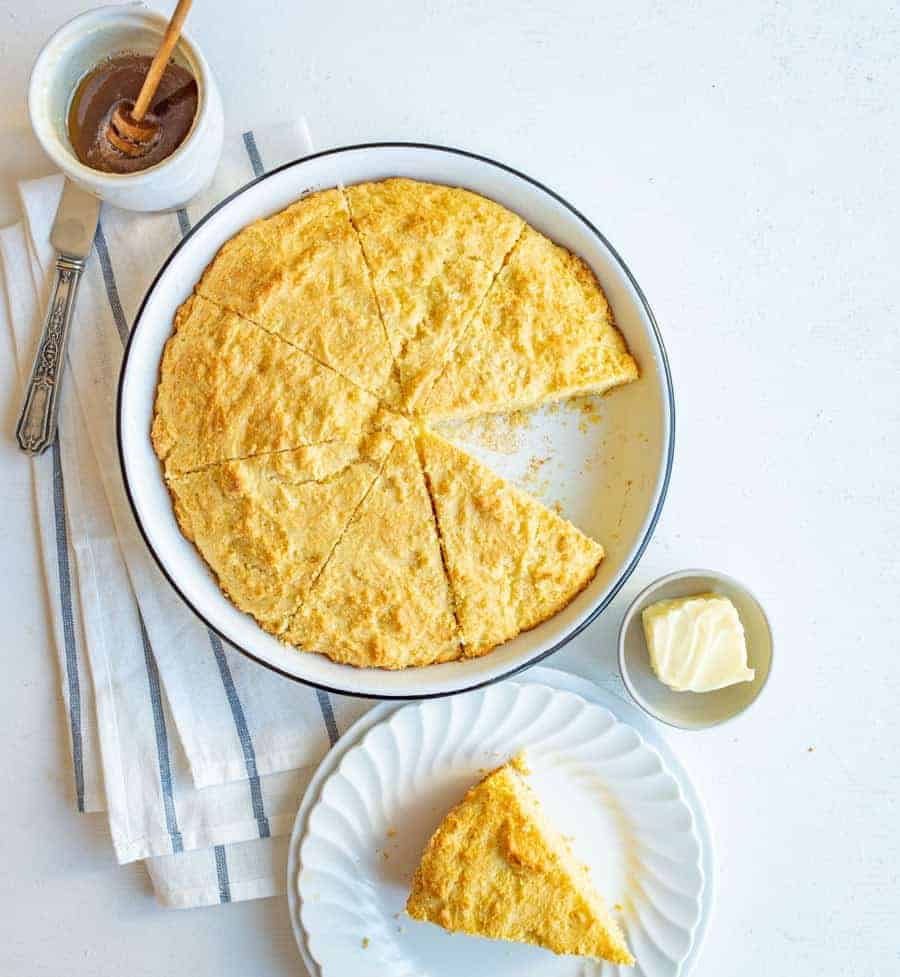 sour cream cornbread in round white dish with piece cutout on white plate with butter and honey.