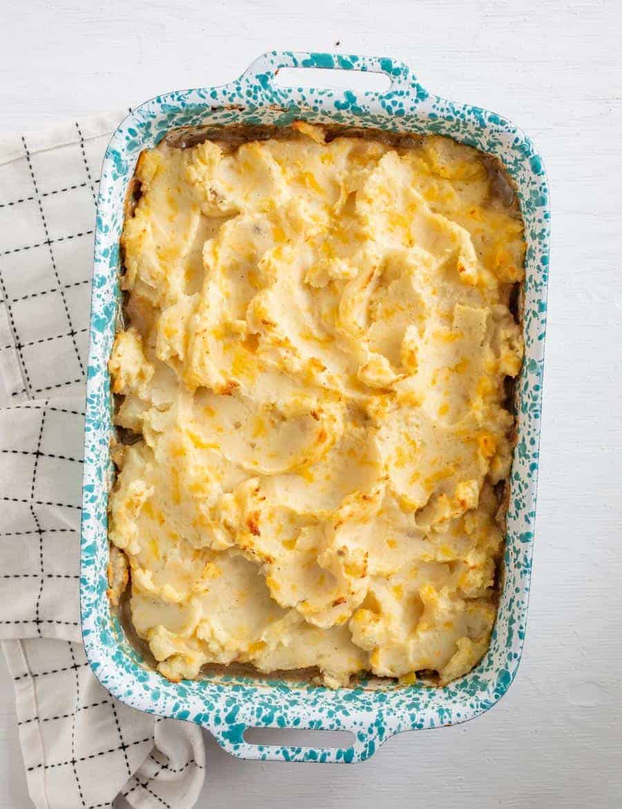 The finished shepherd's pie in a white and blue speckled enamelware pan resting on a white towel with black squares.