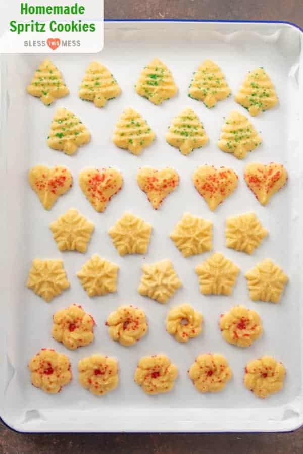 Top view of a parchment-lined baking sheet with four shapes of spritz cookies with red and green sprinkles