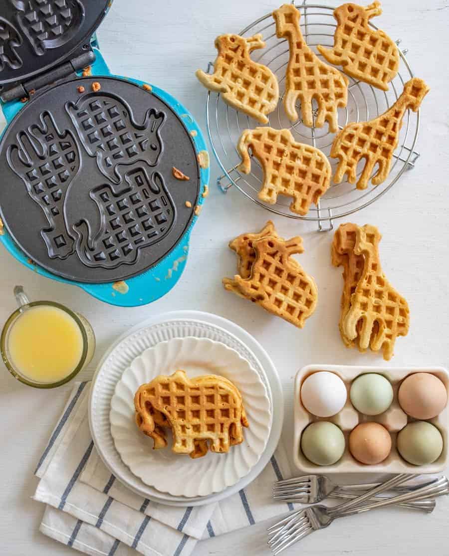 Image of whole wheat waffles in the shape of rabbits, elephants, and giraffes on a wire cooling rack on a white background.
