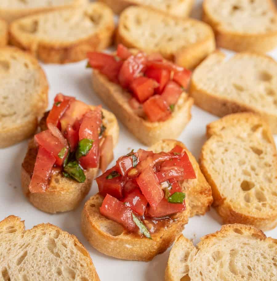 small slices of bread with a few having a pile of cut tomatoes with green pieces of basil.
