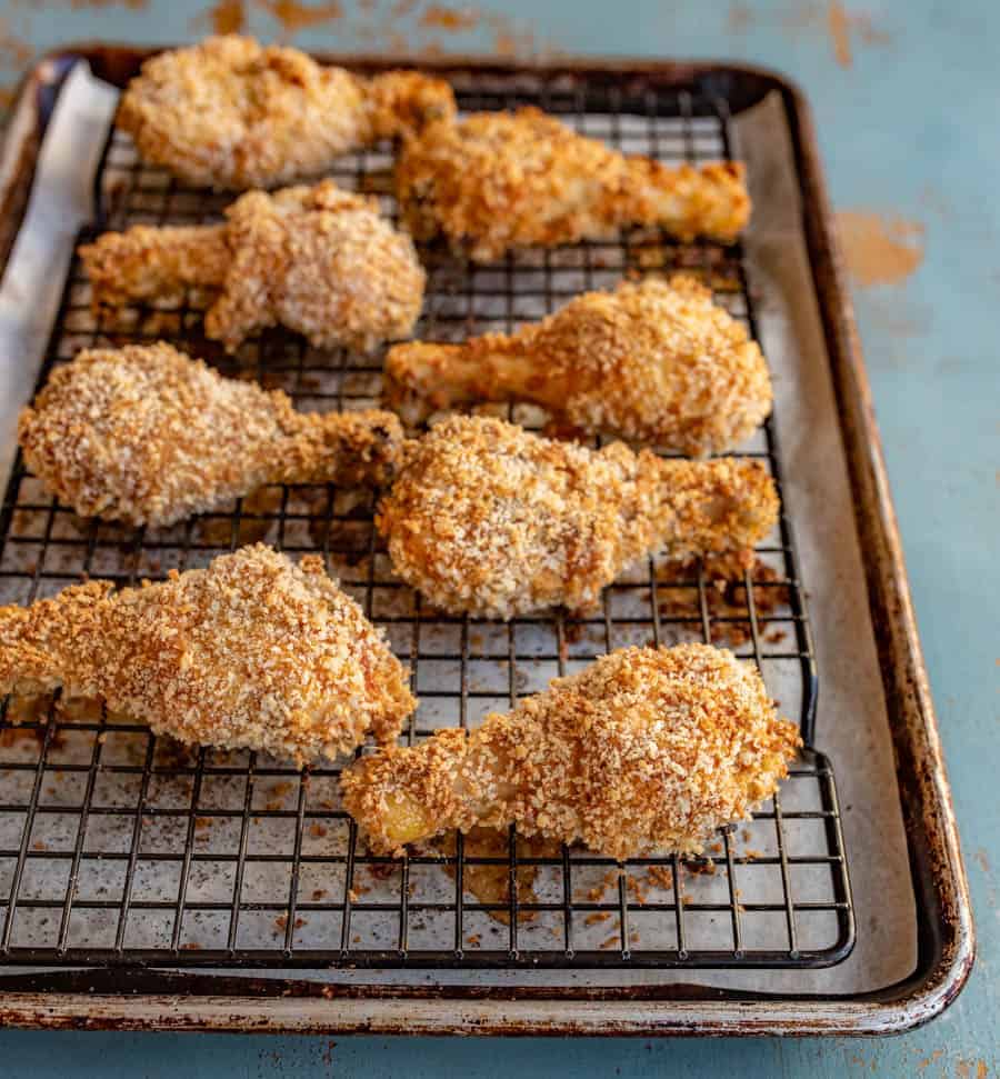 Baked crispy chicken legs sitting on a black wire baking rack inside of a baking pan.