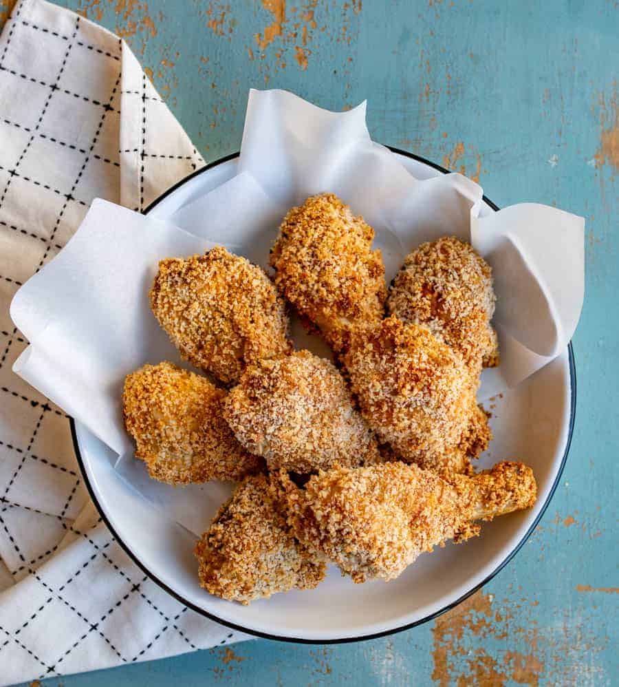 Crispy panko-crusted baked chicken legs in a white bowl with a black rim sitting on a white towel with black lines.