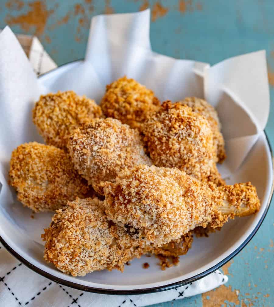 Crispy panko-crusted baked chicken legs in a white bowl with a black rim sitting on a white towel with black lines.