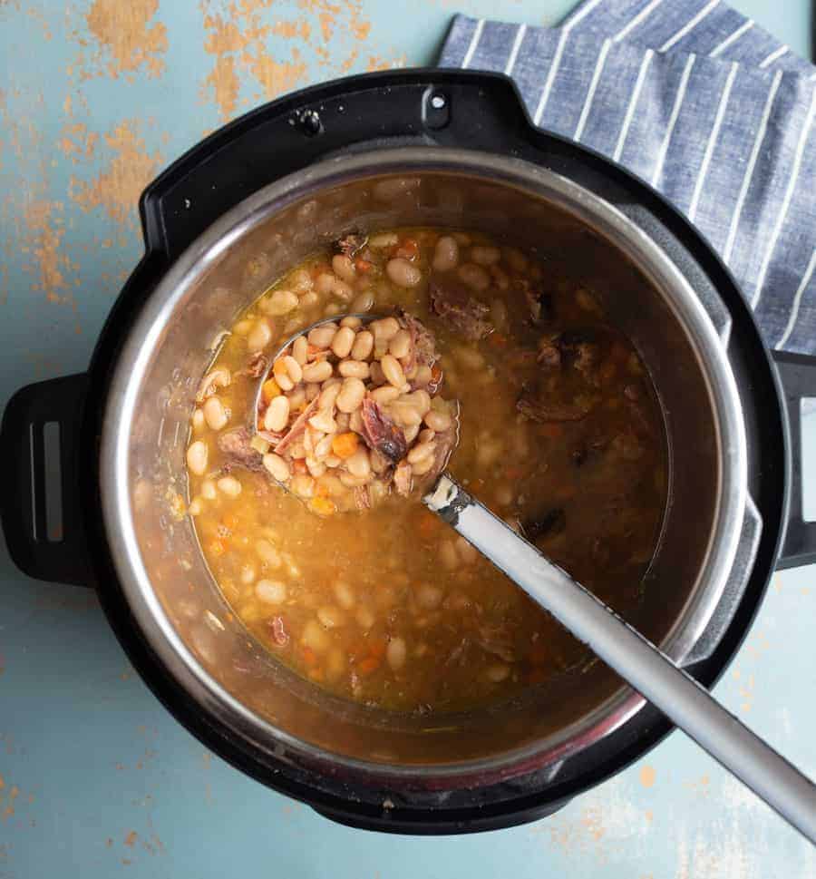 An image of the cooked ham and bean soup in the Instant Pot with a soup ladle in it.