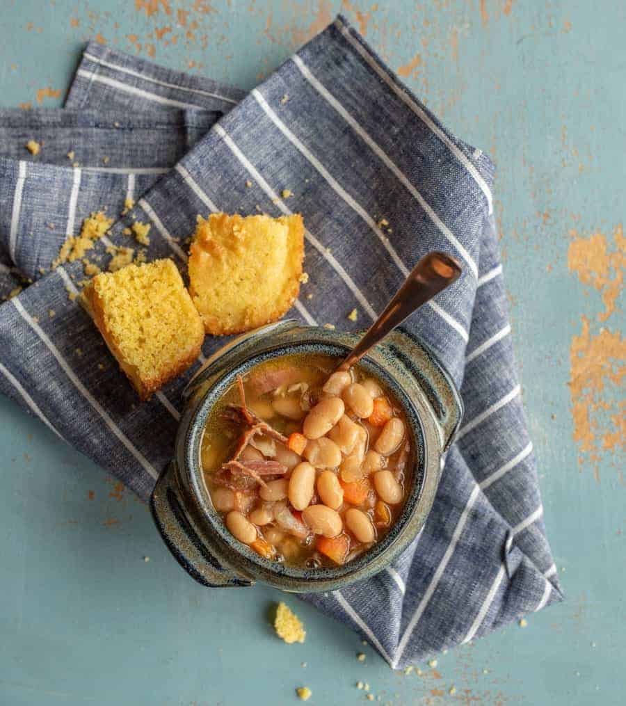 bowl of beans with pieces of cornbread on a blue towel.