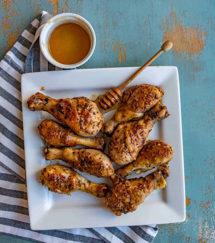 on overhead shot of baked chicken legs on a square dish with a side of honey.