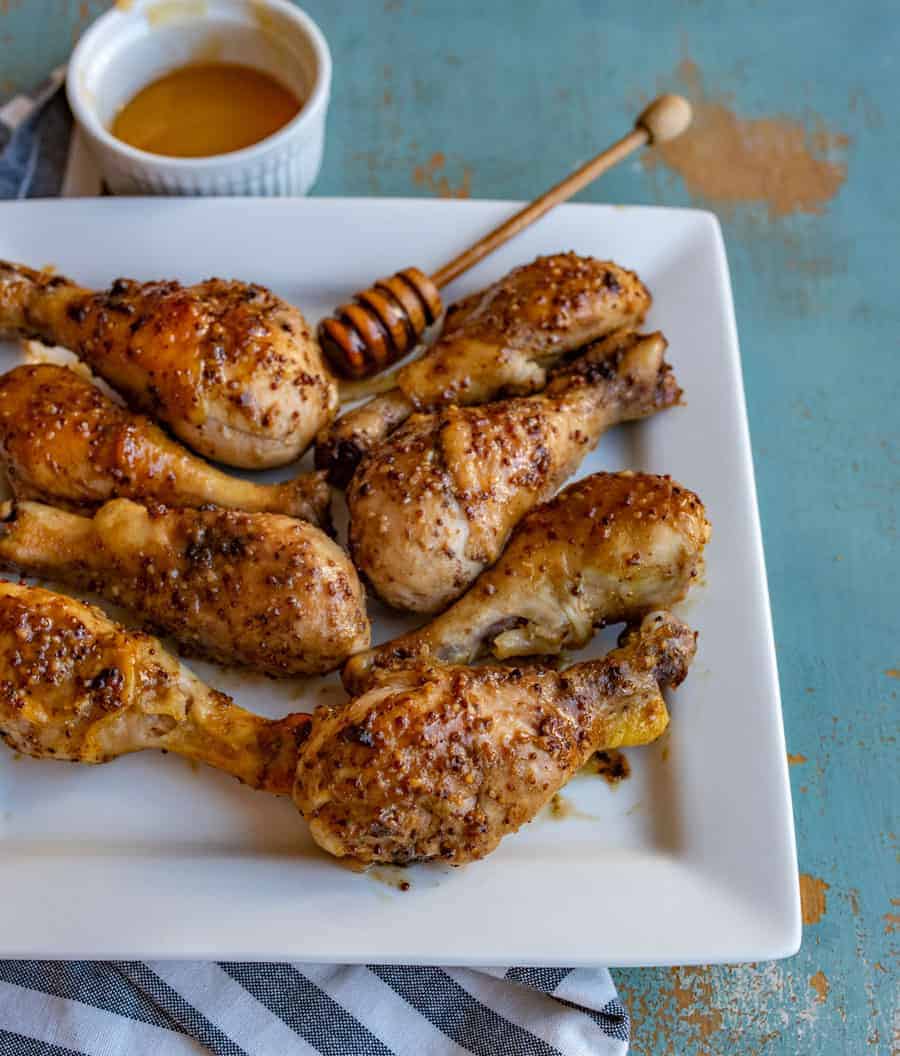 a closeup shot of honey mustard baked chicken legs sitting on a square plate with a side of honey.