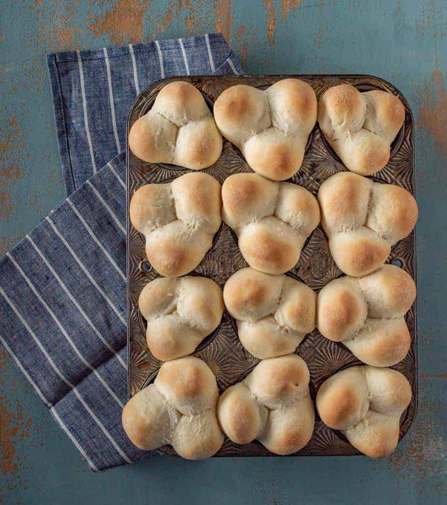 Grandma Lucy's famous clover rolls in muffin pan on white striped blue towel next to stick of butter.