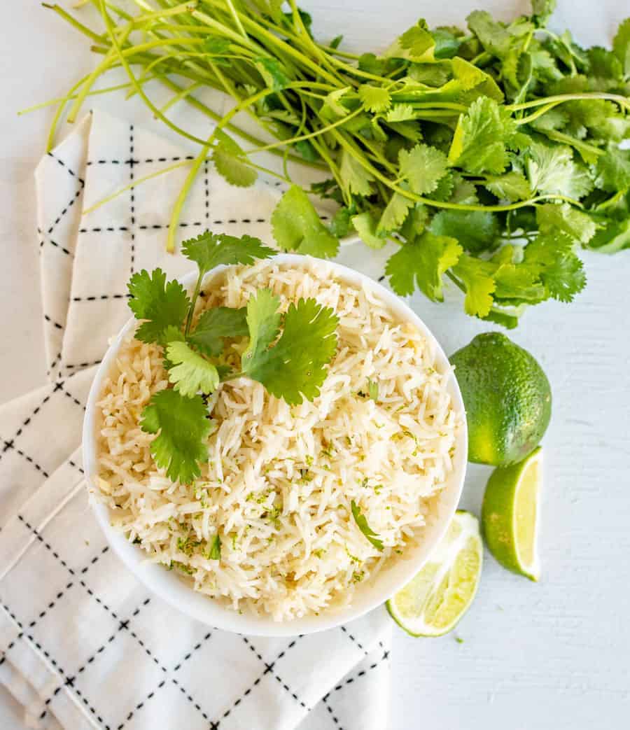 a bowl of cilantro lime rice topped with fresh cilantro. Bowl is surrounded by cilantro and limes.
